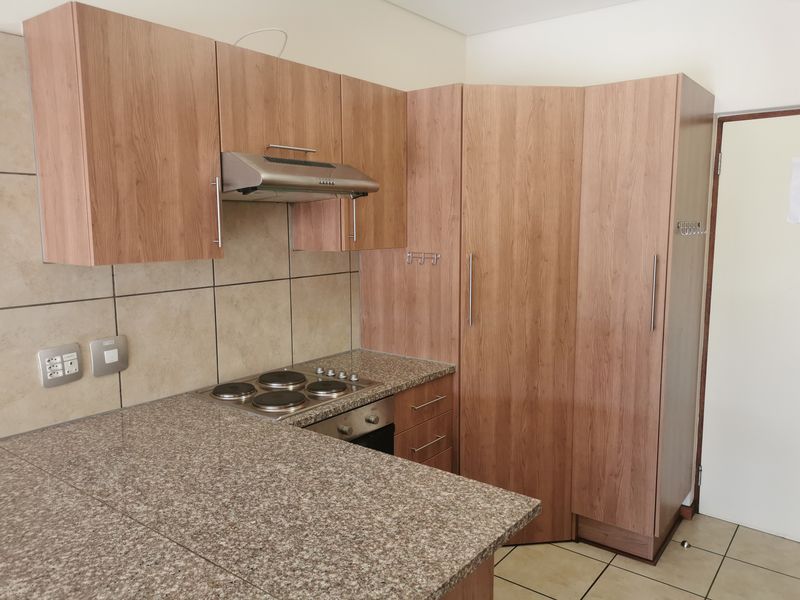 A clean, functional kitchen featuring wood-look laminate cabinetry, granite countertops, a built-in oven, electric hob, and neutral ceramic tile finishes.