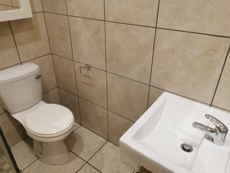A functional bathroom featuring a white toilet, a modern washbasin with a chrome mixer tap, and neutral-toned ceramic wall and floor tiling.