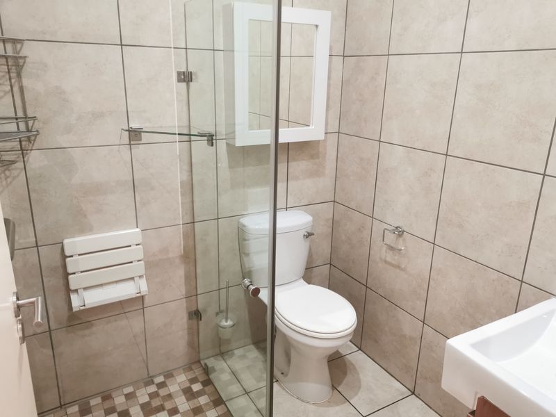 A clean, modern bathroom featuring a walk-in shower with a glass screen, wall-mounted shower seat, toilet, and a wall-mounted medicine cabinet.