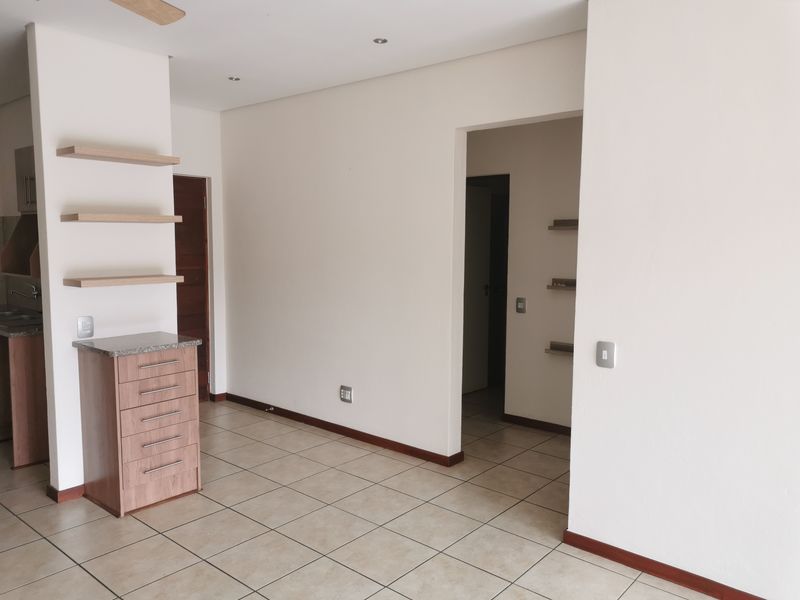 An open-plan living area featuring neutral tiled flooring, built-in cabinetry with granite surfaces, and floating shelving, offering a clean and versatile space.