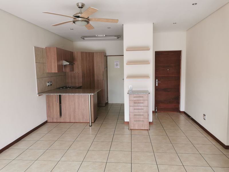 Open plan living area featuring a compact kitchen with built-in cabinetry, hob, extractor fan, and tiled flooring throughout.