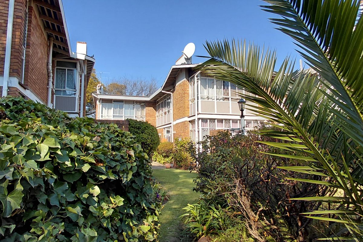 A view of the rear exterior of the townhouse complex, featuring brick facades, enclosed balconies, and a well-maintained garden area.