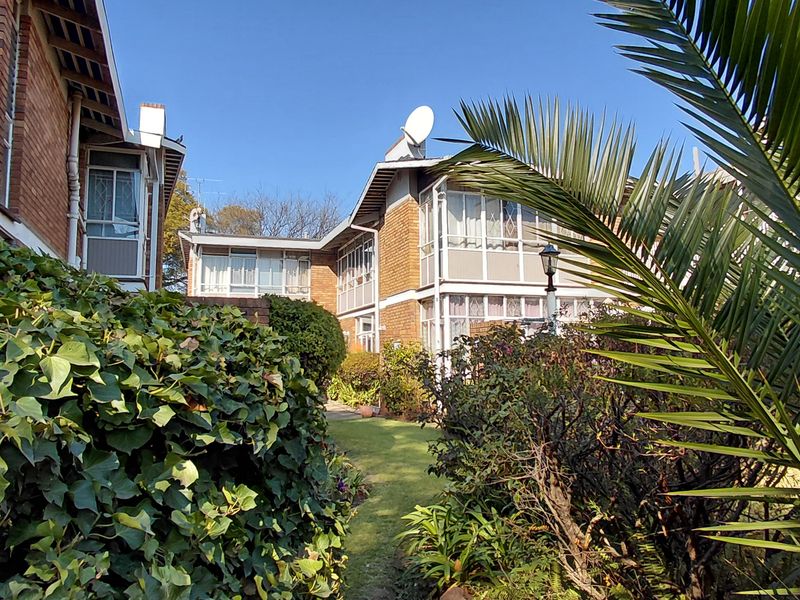 A view of the rear exterior of the townhouse complex, featuring brick facades, enclosed balconies, and a well-maintained garden area.