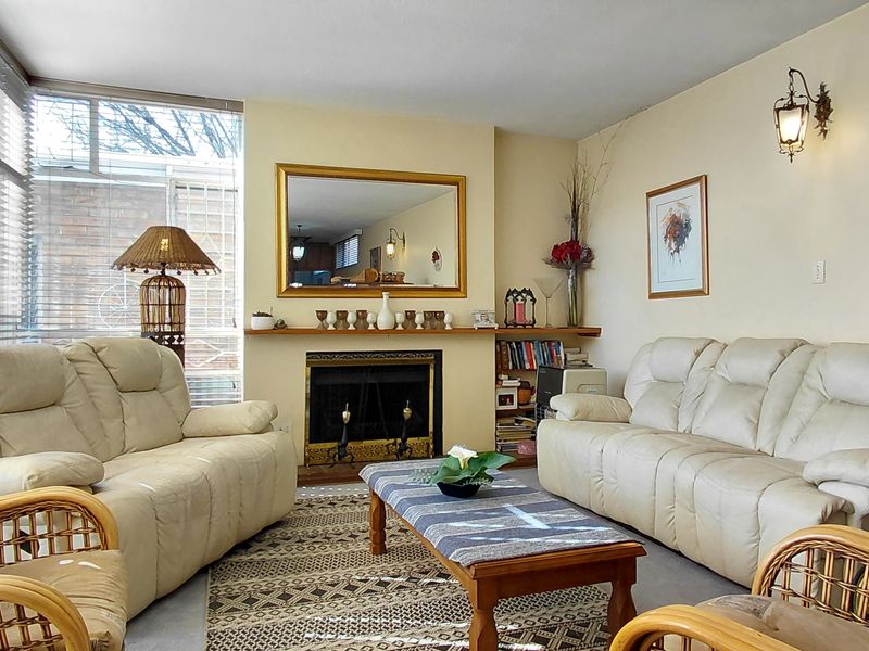 A comfortable living room featuring a central fireplace with a mantelpiece, large windows with venetian blinds, and wall-mounted lighting fixtures.