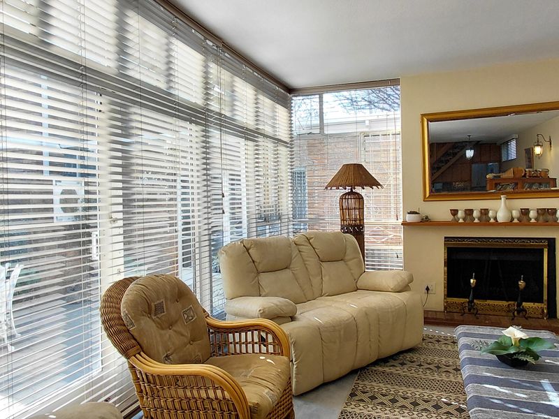 A bright living room featuring a fireplace with a mantelpiece and expansive floor-to-ceiling windows with fitted venetian blinds.