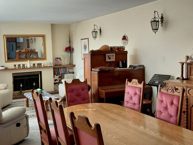 Spacious open-plan living and dining area featuring a fireplace with a mantelpiece, large windows, and classic wall-mounted lighting.