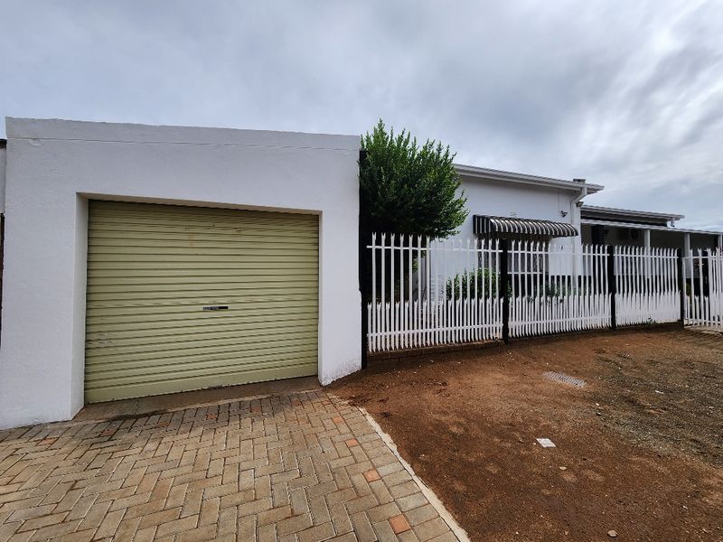 Front exterior view of the property featuring a single roller garage door, paved driveway, and metal security fencing.
