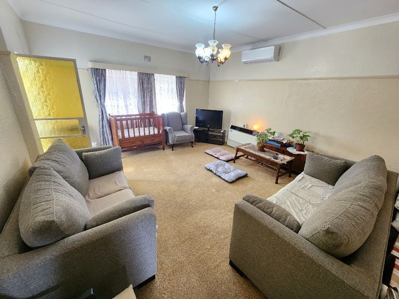 A spacious living room featuring carpet flooring, a split-system air conditioner, and a central chandelier, offering a functional layout for family living.