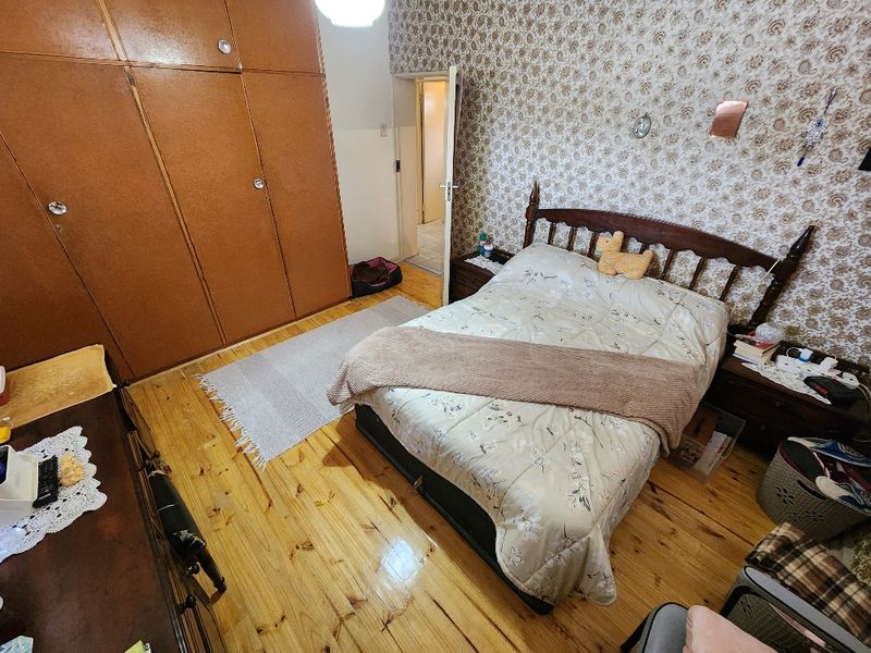 A bedroom featuring timber flooring and built-in cupboards, currently finished with dated wallpaper and requiring cosmetic updates to modernize the space.