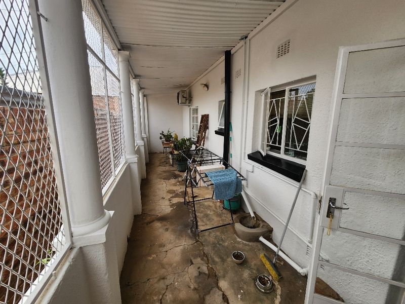 A covered outdoor patio area featuring concrete flooring, security mesh enclosure, and structural columns, providing a functional utility space along the side of the house.