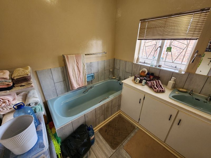 A functional bathroom featuring a built-in bathtub, vanity cabinet with integrated sink, and tiled splashback, offering potential for modernization and cosmetic updates.