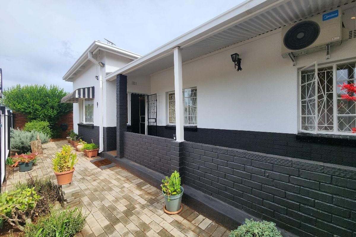 A well-maintained rear exterior view featuring a covered patio, paved walkway, and secure window bars, complemented by a clean painted brick facade.