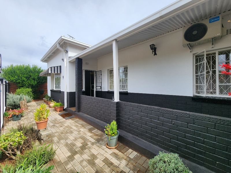 A well-maintained rear exterior view featuring a covered patio, paved walkway, and secure window bars, complemented by a clean painted brick facade.