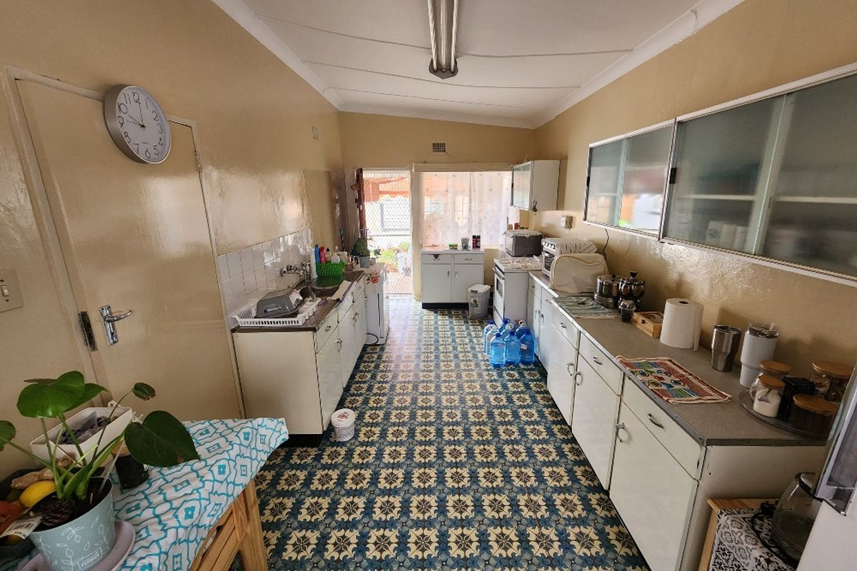 A functional, dated kitchen featuring original cabinetry, patterned tile flooring, and a stainless steel sink, offering significant potential for a modern renovation.