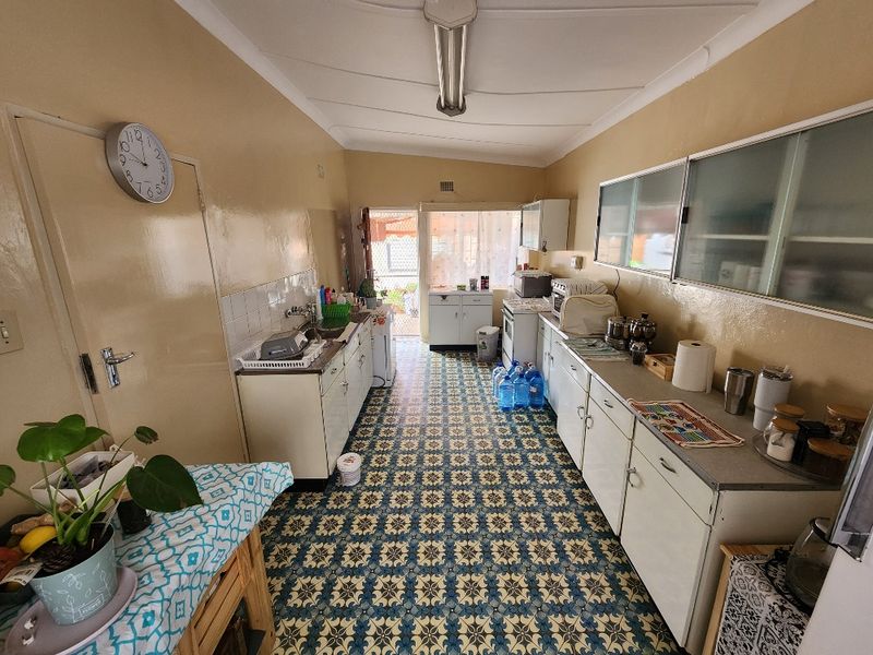 A functional, dated kitchen featuring original cabinetry, patterned tile flooring, and a stainless steel sink, offering significant potential for a modern renovation.