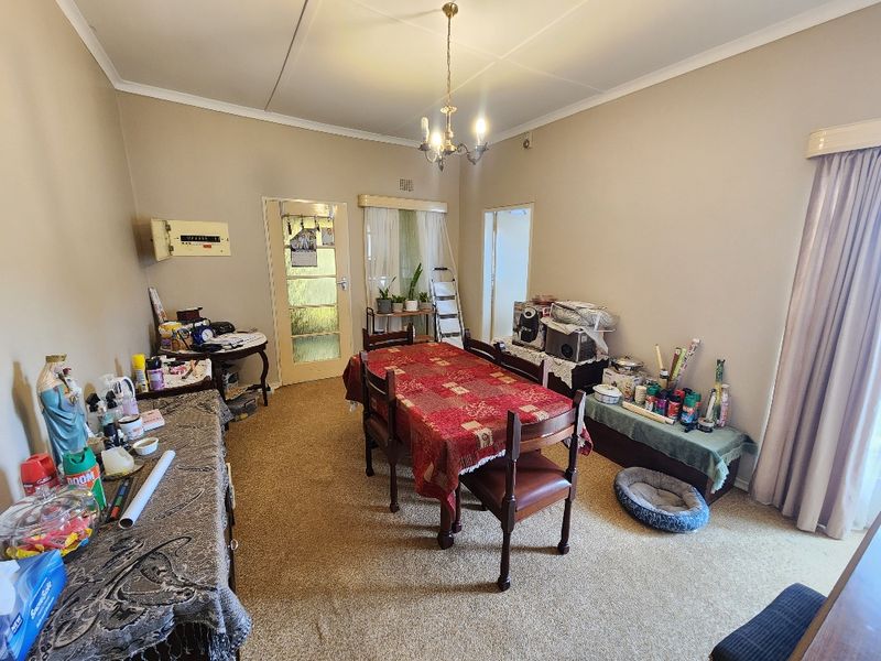 A dining room featuring a central chandelier, carpeted flooring, and a glass panel door, offering a functional space for family meals.