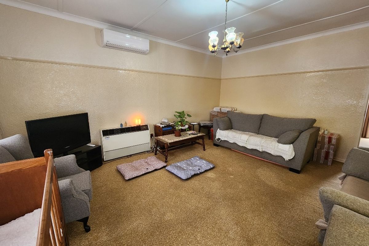 A spacious living room featuring carpet flooring, a wall-mounted heater, and a split-system air conditioner for climate control.