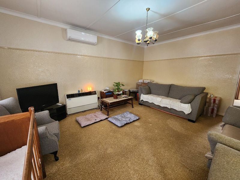 A spacious living room featuring carpet flooring, a wall-mounted heater, and a split-system air conditioner for climate control.