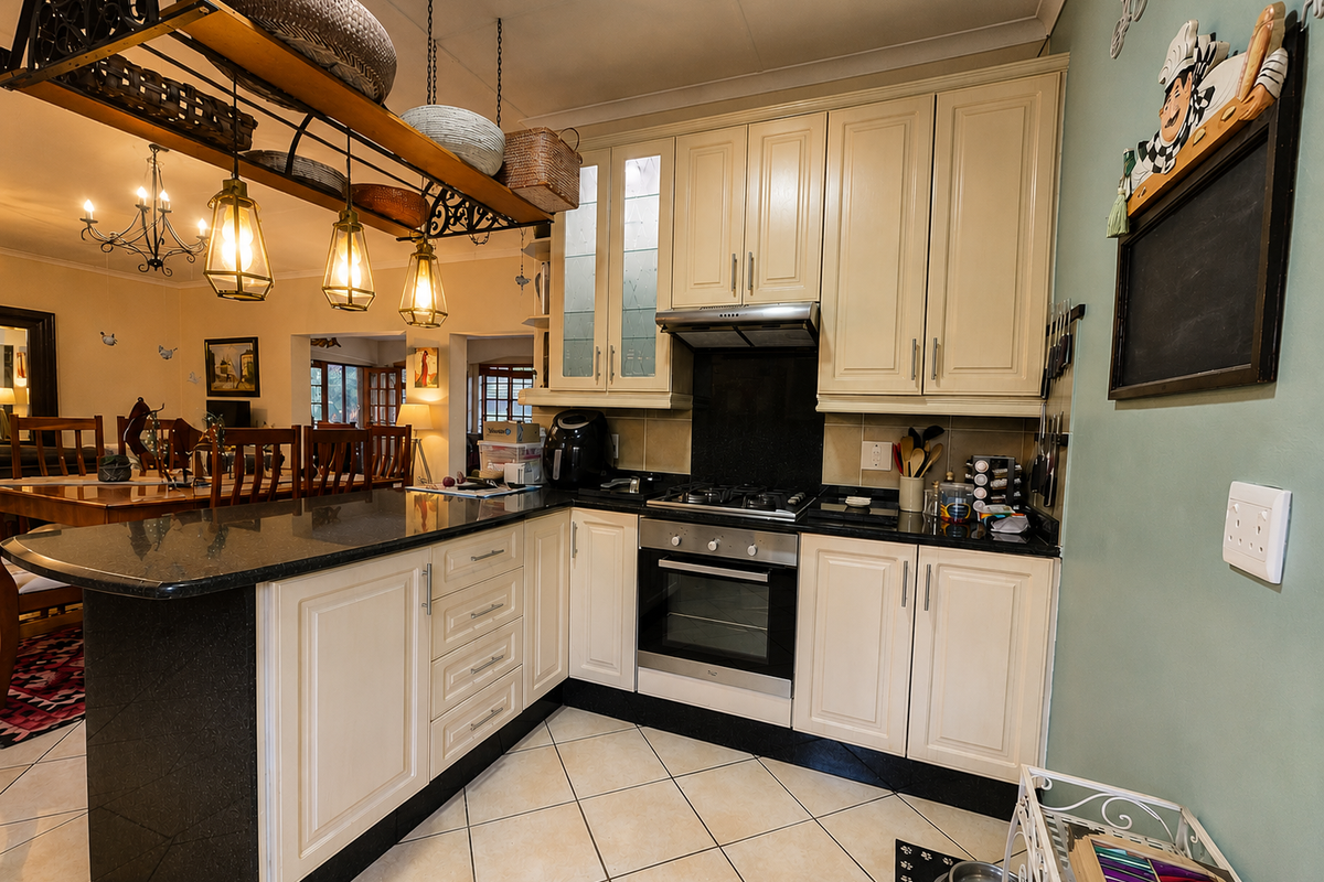 A well-maintained kitchen featuring cream cabinetry, granite countertops, a built-in oven with gas hob, and an integrated breakfast bar overlooking the dining area.