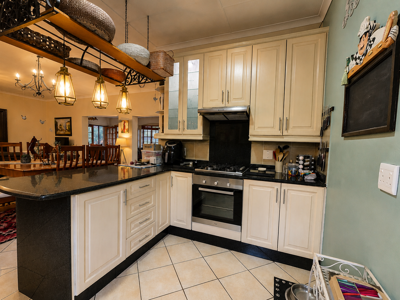 A well-maintained kitchen featuring cream cabinetry, granite countertops, a built-in oven with gas hob, and an integrated breakfast bar overlooking the dining area.