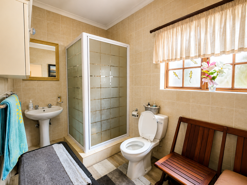 A functional bathroom featuring a pedestal basin, a corner shower enclosure, and a toilet, finished with neutral wall and floor tiling.