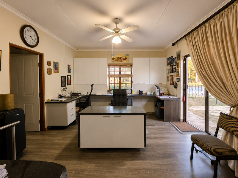 A functional home office featuring built-in cabinetry, a central desk, ceiling fan, and direct access to the outdoor area through a sliding glass door.