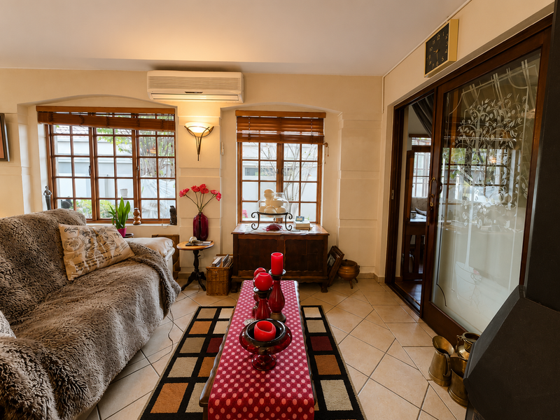 A cozy living room featuring tiled flooring, a split-system air conditioner, wood-framed windows, and a sliding glass door leading to an adjacent space.