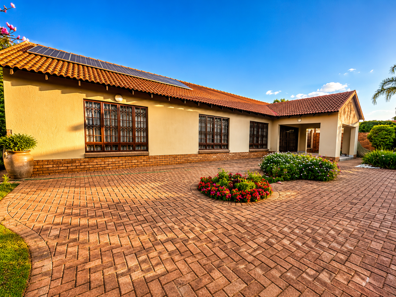 Front elevation of a well-maintained townhouse featuring a tiled roof with solar panels, brick paving, and secure window treatments.