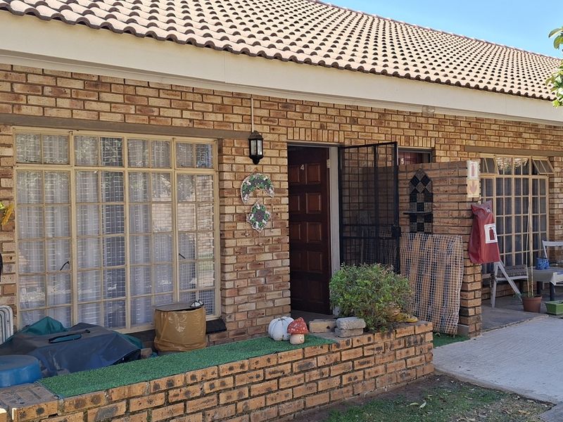 Front elevation of a face brick townhouse featuring a tiled roof, steel window frames, and a secure entrance door with a security gate.