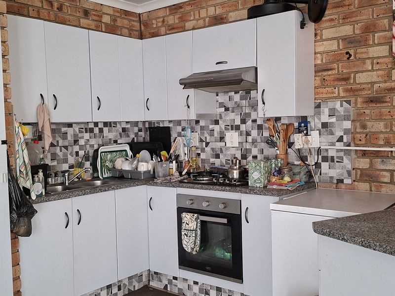A functional kitchen featuring white cabinetry, granite-look laminate countertops, a built-in oven with gas hob, and a distinctive exposed brick feature wall.