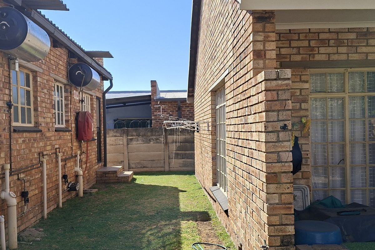Rear exterior view of the townhouse featuring face brick walls, external geysers, and a small garden area between the building structures.