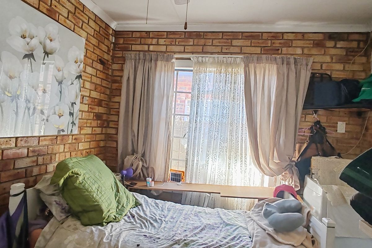 A bedroom featuring exposed brick walls and a window, offering a rustic aesthetic with potential for modernization.