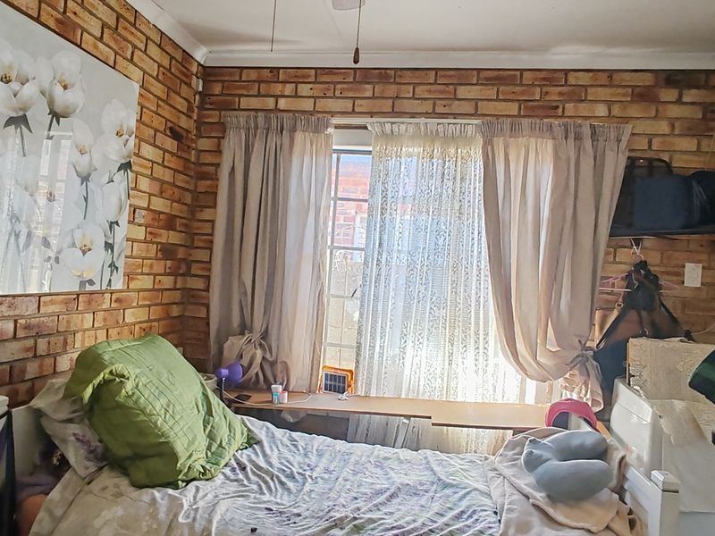 A bedroom featuring exposed brick walls and a window, offering a rustic aesthetic with potential for modernization.
