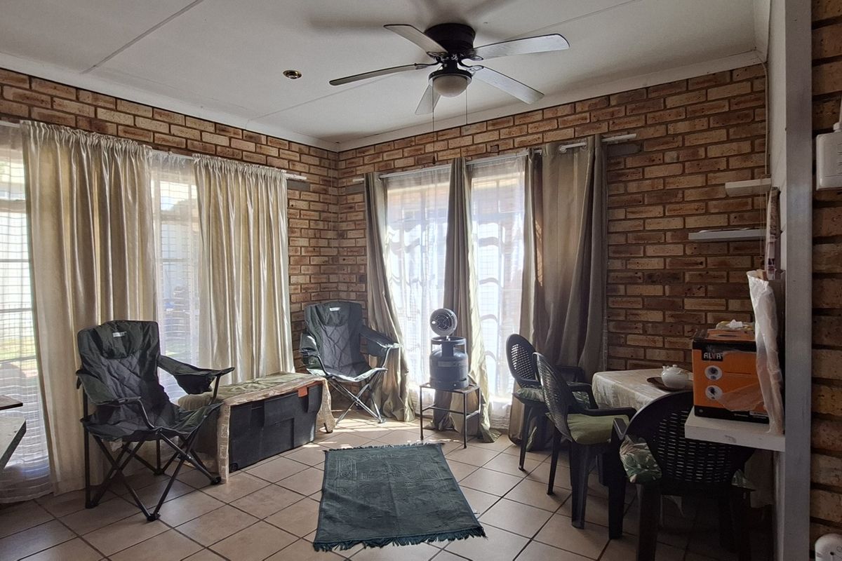 A living room featuring exposed brick walls, tiled flooring, and a ceiling fan, with sliding glass doors providing natural light.