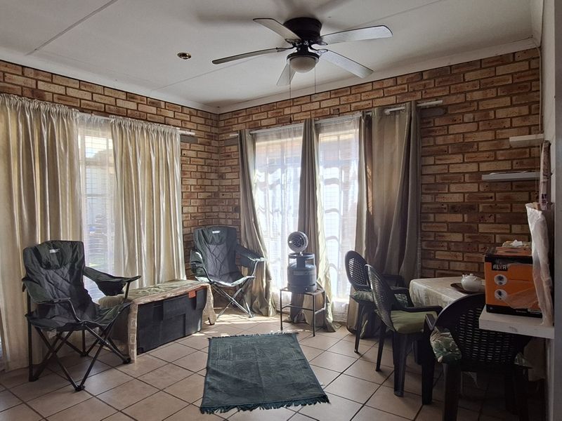 A living room featuring exposed brick walls, tiled flooring, and a ceiling fan, with sliding glass doors providing natural light.