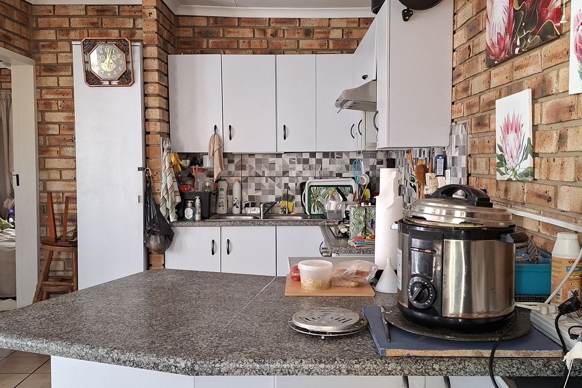 A functional kitchen featuring exposed brick walls, white cabinetry, mosaic tile backsplash, and a granite-look laminate countertop.