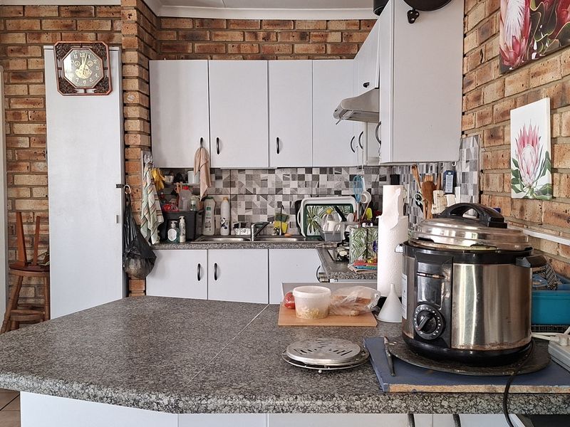 A functional kitchen featuring exposed brick walls, white cabinetry, mosaic tile backsplash, and a granite-look laminate countertop.