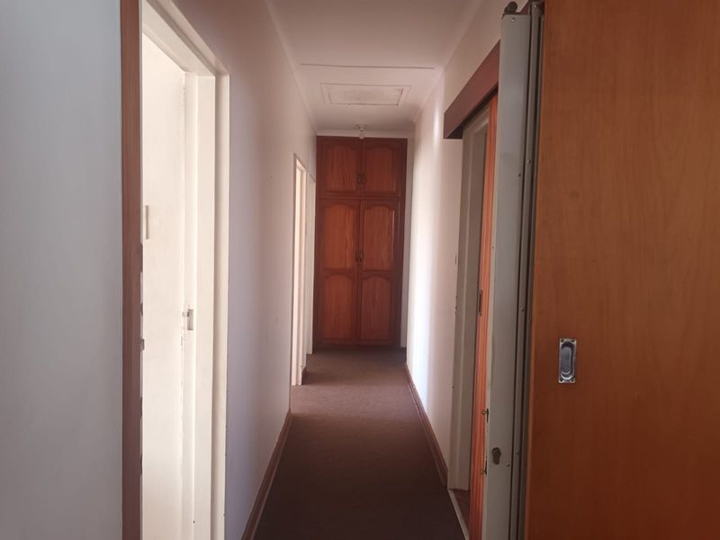 A functional hallway featuring carpeted flooring and a built-in wooden cupboard at the end, providing access to multiple rooms.