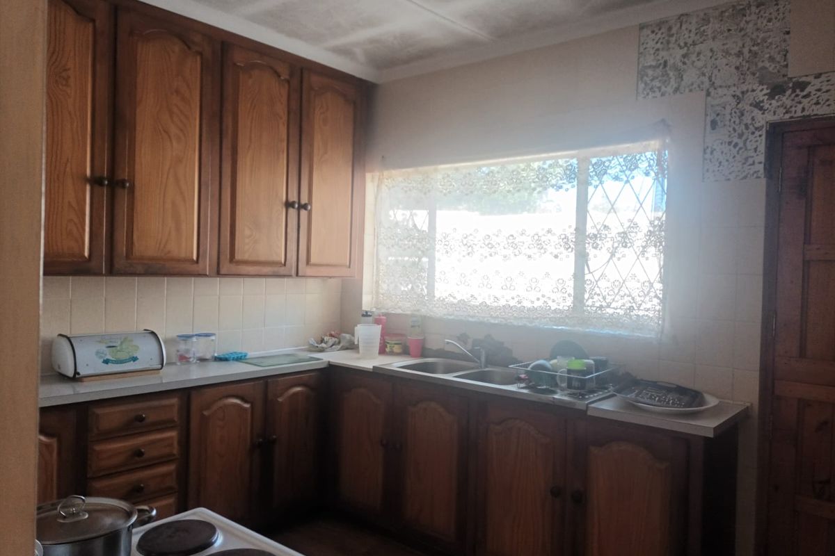 A dated kitchen featuring wooden cabinetry, laminate countertops, a double basin sink, and an electric stove, requiring cosmetic updates to modernize the space.