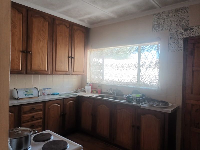 A dated kitchen featuring wooden cabinetry, laminate countertops, a double basin sink, and an electric stove, requiring cosmetic updates to modernize the space.