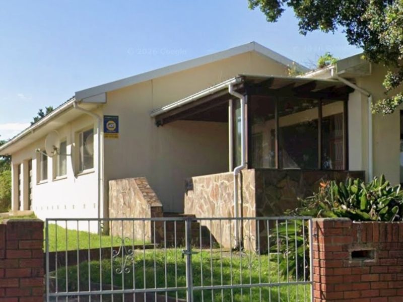 Front view of a single-story house featuring a brick boundary wall, metal gate, and a covered patio area with stone cladding.