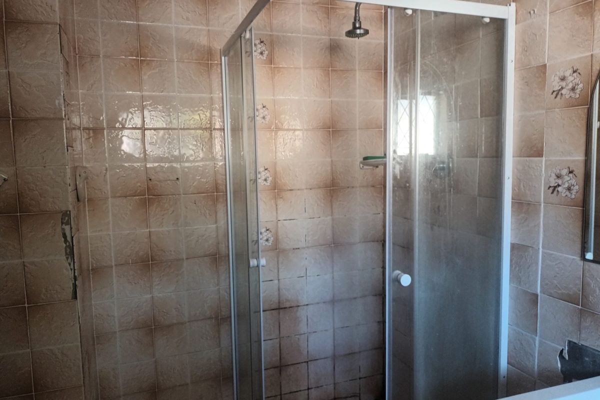 A bathroom featuring a glass shower enclosure and dated ceramic wall tiling, requiring cosmetic updates to improve the overall aesthetic.
