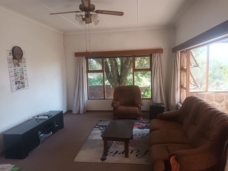 A spacious living room featuring large windows that provide natural light and a view of the garden, complemented by a ceiling fan.