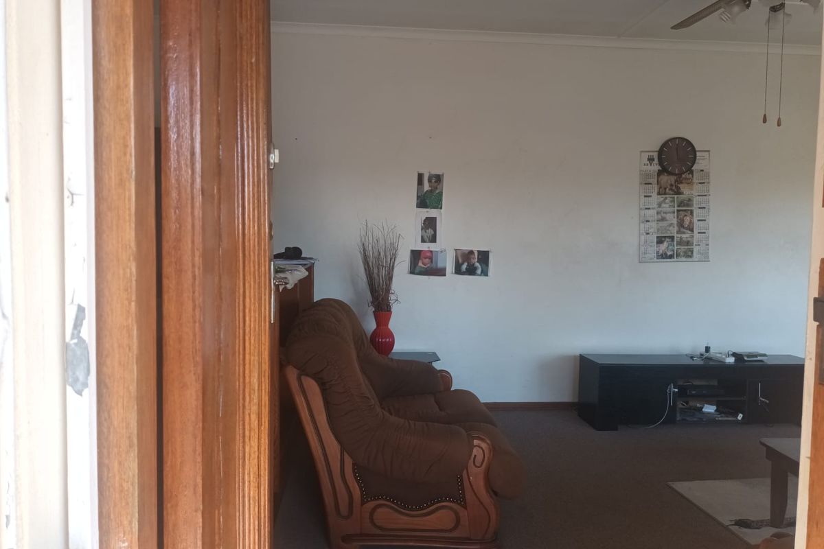 A living room area featuring a ceiling fan and carpeted flooring, viewed through a wooden door frame.