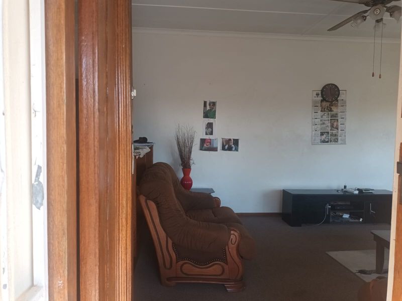 A living room area featuring a ceiling fan and carpeted flooring, viewed through a wooden door frame.