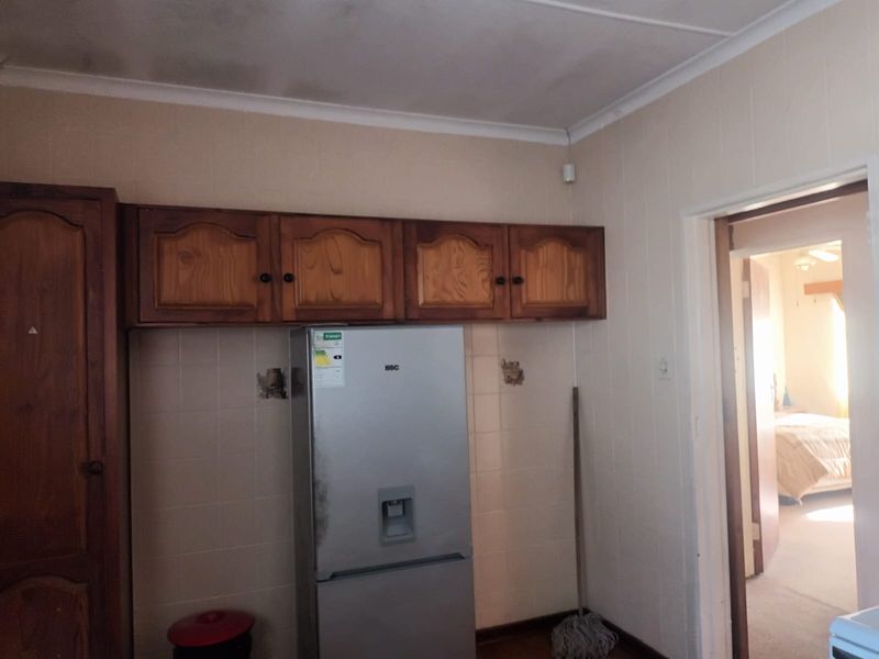 A kitchen area featuring wooden wall-mounted cabinetry and tiled splashbacks, requiring some cosmetic updates to the ceiling and wall finishes.