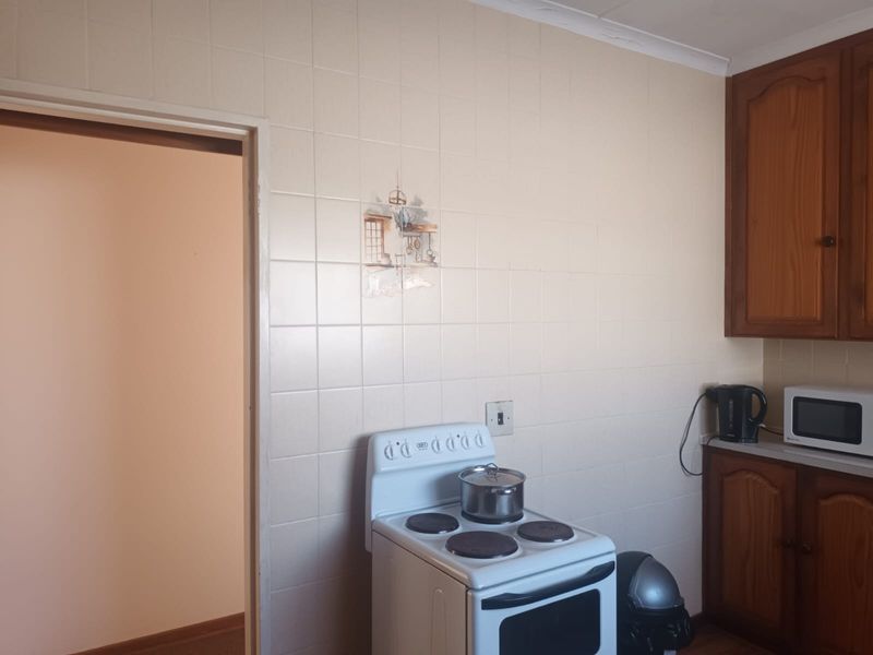 A dated kitchen featuring traditional wooden cabinetry, tiled splashbacks, and a freestanding electric stove, offering potential for a modern renovation.