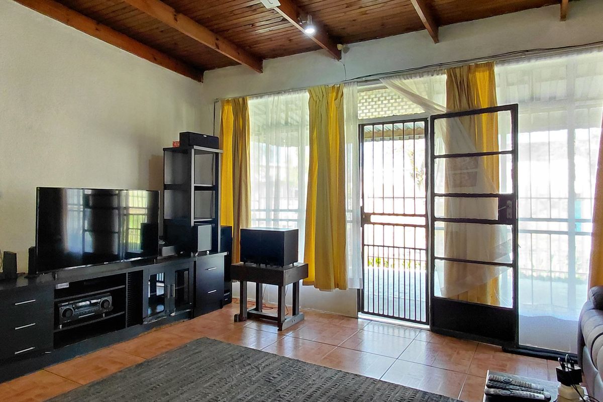 Living room featuring exposed timber beam ceilings, tiled flooring, and direct access to the exterior through a security gate and sliding glass door.