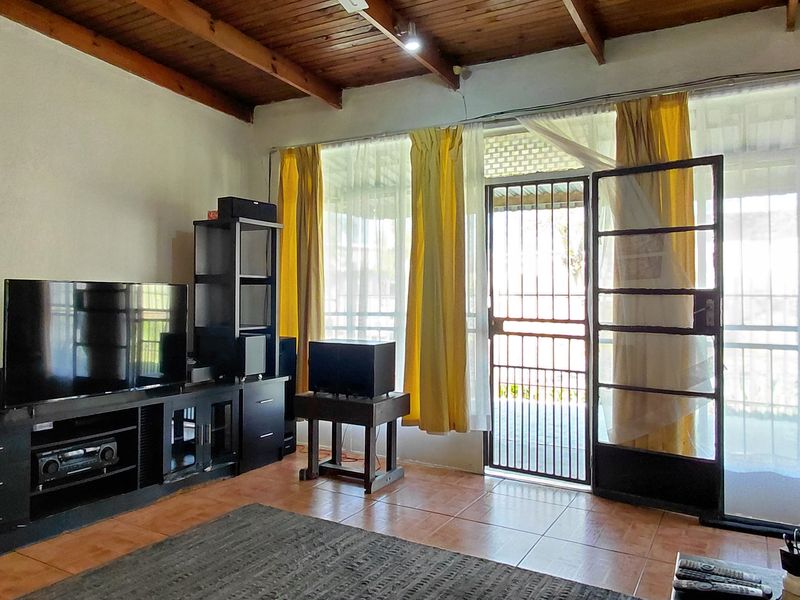 Living room featuring exposed timber beam ceilings, tiled flooring, and direct access to the exterior through a security gate and sliding glass door.