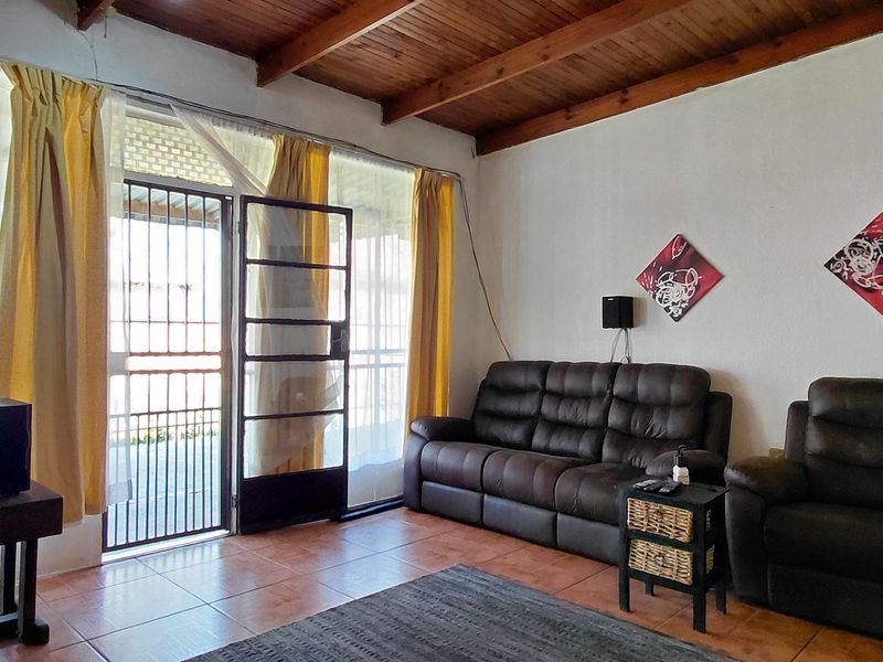 A living room featuring exposed timber ceiling beams, tiled flooring, and a sliding glass door with an integrated security gate leading to the exterior.